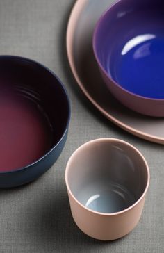 three different colored bowls sitting next to each other on top of a gray tablecloth