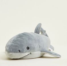 a gray stuffed shark laying on top of a white surface with its mouth open and tongue out