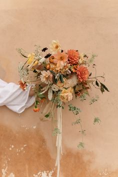 a bridal bouquet with peach and white flowers on a wall in front of a building