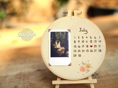 an embroidered photo frame with a calendar on it and the date for july is shown