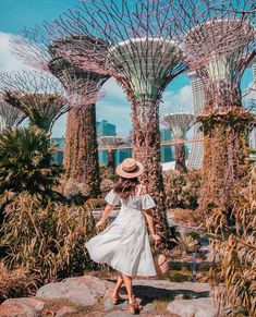 a woman in a white dress and straw hat walks through the gardens by the bay