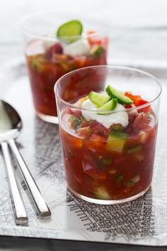 two glasses filled with food sitting on top of a white tray next to spoons