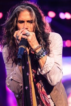 a man with long hair holding a microphone in his hand and singing into the microphone