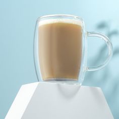 there is a cup of coffee sitting on top of a white stand with a blue wall in the background