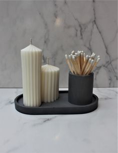 two candles are sitting on a tray next to some matchesticks in a cup