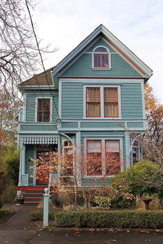 a blue house with red trim on the front and side windows, in autumn time