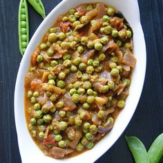 a bowl filled with peas and carrots on top of a table next to green beans