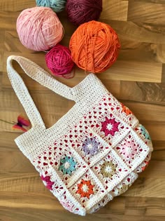 crochet granny bag with balls of yarn on the floor next to it and two skeins of yarn