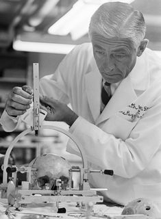 a black and white photo of a man in a lab coat working on a skull