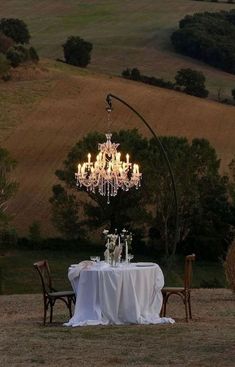 a dining table set for two with chandelier in the middle and chairs around it