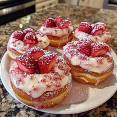 four donuts covered in powdered sugar and topped with strawberries on a plate