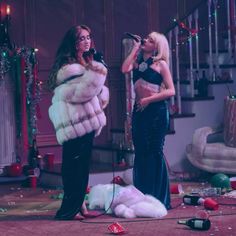 two women singing into microphones in front of christmas decorations and confetti on the floor