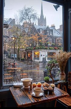 two cups of coffee sit on a table in front of an open window overlooking the city