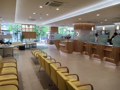 an empty waiting area with yellow chairs and people in the background at the front desk