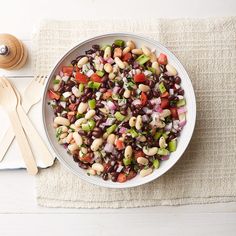 a white bowl filled with beans and veggies next to wooden utensils