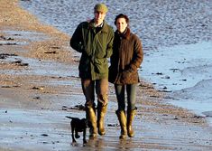 a man and woman are walking along the beach with their dog on a cold day