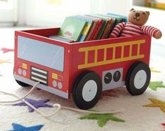 a wooden toy fire truck with books in it on the floor next to a teddy bear