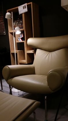 a tan leather chair and foot stool in a room with shelves on the wall behind it