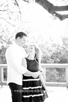 a man and woman standing next to each other under a tree in black and white