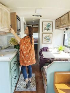 a woman standing in the kitchen area of a travel trailer