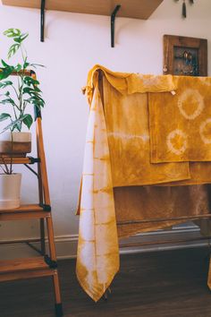 a yellow towel hanging on a rack next to a potted plant and wooden chair