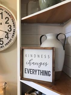 a white clock sitting on top of a wooden shelf next to a sign that says kindness changes everything