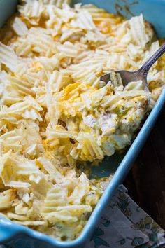 a blue casserole dish filled with chicken and cheese, topped with a spoon