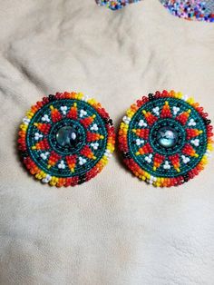 two colorful beaded earrings sitting on top of a white cloth covered bed next to each other