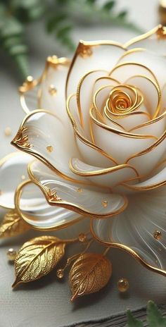 a white and gold rose with leaves on it's side sitting on a table