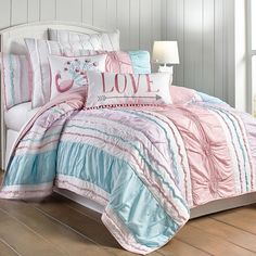 a bed with pink, blue and white comforter set on top of wooden floor