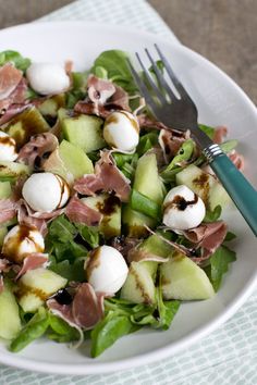 a white plate topped with salad covered in meat and veggies next to a fork