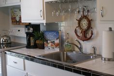 a kitchen with white cabinets and stainless steel sink under a clock mounted on the wall