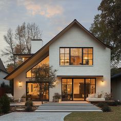 a white house with large windows and steps leading up to the front door at dusk