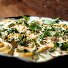 a pizza with spinach, cheese and sauce in a pan on a wooden table