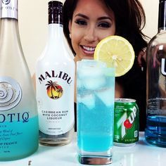 a woman sitting at a table with several bottles and glasses next to her, smiling