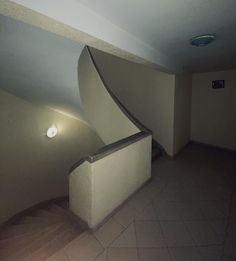 an empty room with a curved staircase and light fixture on the wall, next to a tiled floor