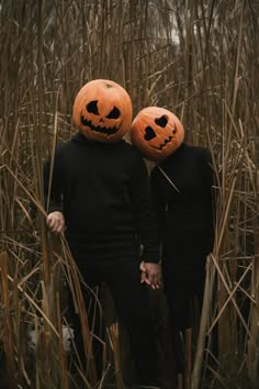 two people wearing pumpkin heads standing in tall grass