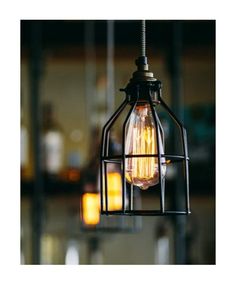 an old fashioned light bulb hanging from a wire cage with lights in the back ground