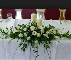 white roses and greenery are arranged on the centerpiece of a table at a wedding reception