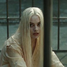 a woman with long white hair sitting in front of a fence and looking at the camera