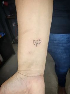 a small tattoo on the wrist of a person's left arm, with a bird flying above it