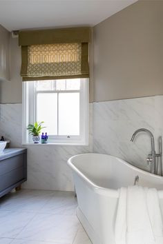 a white bath tub sitting under a window next to a sink in a room with marble floors