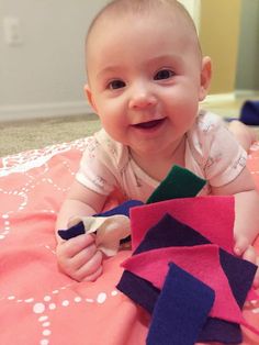 a baby is laying on the floor and playing with some fabric pieces that have been cut into shapes