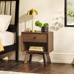 a night stand with books and a lamp on it next to a bed in a bedroom