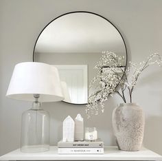 a white table topped with a vase filled with flowers next to a mirror and lamp