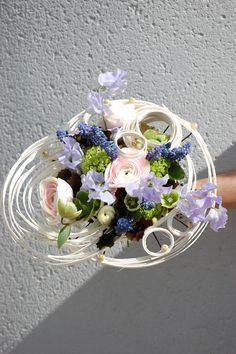 a bouquet of flowers is held in a white wire basket against a gray painted wall