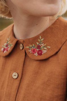 a woman with blonde hair wearing an orange shirt and flower embroidered on the collarline