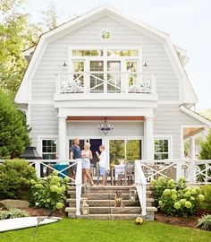 two people are standing on the front porch of a white house with stairs leading up to it