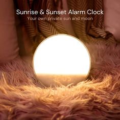 an alarm clock sitting on top of a furry floor next to pillows and blankets with the words sunrise & sunset alarm clock