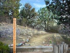 a wooden bench sitting on the side of a dirt road next to a wooded hillside